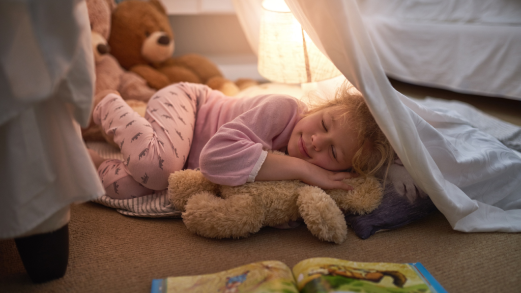 Small child sleeping with her teddy bear inside her home made fort